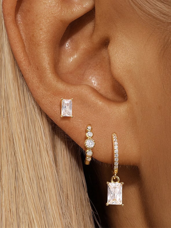 Elegante Damenohrringe aus 925er Sterlingsilber mit Zirkonia – rechteckiger Ohrstecker, funkelnder Ear Cuff mit runden Steinen und goldene Creole mit Anhänger, getragen an einem weiblichen Ohr.